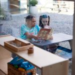 Montessori Book Buddies program at Fraser Woods School Newtown CT with older student mentoring younger student during reading session near classroom window with Montessori materials visible